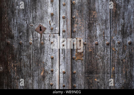 Spanische antike hölzerne Tür: Close-up der rostigen Griff, das Schloss und Nieten. Rauhe graue Holzoberfläche mit gerissenen Hintergrund Muster. Stockfoto