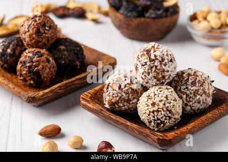 Gesunde Energie Kugeln von Nüssen, oatmeals und getrocknete Früchte mit Kokosnuss, Leinsamen und Sesam auf hölzernen coconut Platten auf einem weißen Hintergrund, horizontal Stockfoto