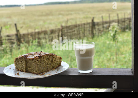 Brötchen mit Mohnsamen mit einem Glas Milch. Milch in ein Glas und Mohn Kuchen auf einem Feld Hintergrund. Torte mit einer Tasse Milch in das Dorf auf dem Bac Stockfoto
