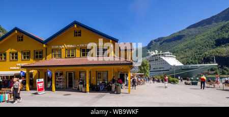 Touristen in Flåm, FABRIK KUTSALG FACTORY OUTLET, Geschäfte, gelbes Holzhaus, Ausflug Schiff, Fjord, Gebirge, Bäume, blauer Himmel, Sogn og Fjordane, Norwa Stockfoto