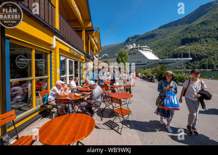 Touristen in Flåm, FABRIK KUTSALG FACTORY OUTLET, ein Café, ein gelbes Holzhaus, Ausflug Schiff, Fjord, Gebirge, Bäume, blauer Himmel, Sogn og Fjordane, Norwegen Stockfoto