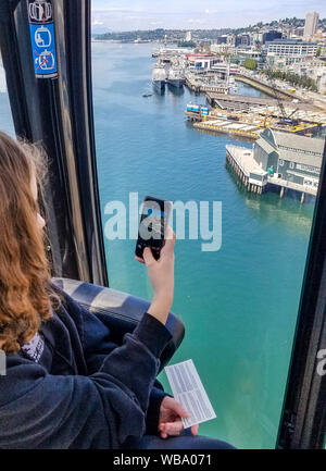 Junge Jugendmädchen fotos Downtown Seattle mit ihrem Handy aus Seattle's große Rad, eine Gondelfahrt am Ende der Pier 57 im Elliot Bay. Mit einer Gesamthöhe von 175 Metern, war es das höchste Riesenrad an der Westküste der Vereinigten Staaten, wenn es am 29. Juni 2012 geöffnet. Einer der Seattle touristischen Boote kommt im Dock und ein Seattle ferry kann im Hintergrund gesehen werden. Stockfoto