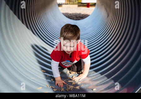 Ein kleiner Junge kriecht durch einen Spielplatz Tunnel, Entdecken und Spaß haben Stockfoto