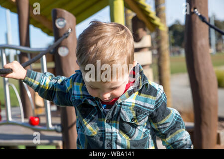 Ein kleiner Junge sorgfältig Praktiken, die über die Hängebrücke auf dem Spielplatz fort Stockfoto