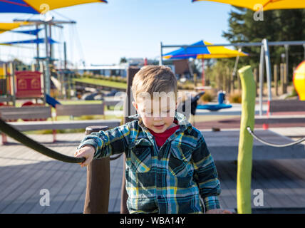 Ein kleiner Junge sorgfältig Praktiken, die über die Hängebrücke auf dem Spielplatz fort Stockfoto