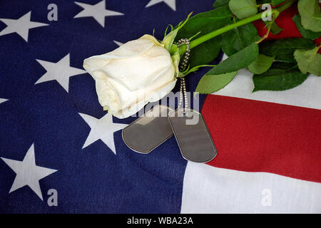 Nahaufnahme der Einzelne weiße Rose und militärischen Dog Tags auf amerikanische Flagge Stockfoto