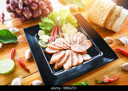 Gegrillte würstchen Schweinefleisch in Scheiben geschnitten gebackenes Schweinefleisch gebraten mit klebrigem Reis Kräuter und Gewürze Zutaten frisches Gemüse auf dem Teller in den hölzernen Tisch serviert. Stockfoto