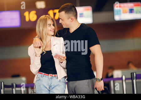 Paar in einem Flughafen. Schöne Blondine in einem weißen Mantel. Mann in einem schwarzen T-Shirt Stockfoto