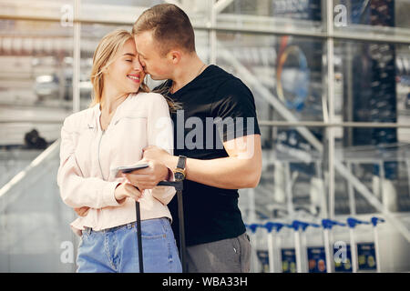 Paar in einem Flughafen. Schöne Blondine in einem weißen Mantel. Mann in einem schwarzen T-Shirt Stockfoto