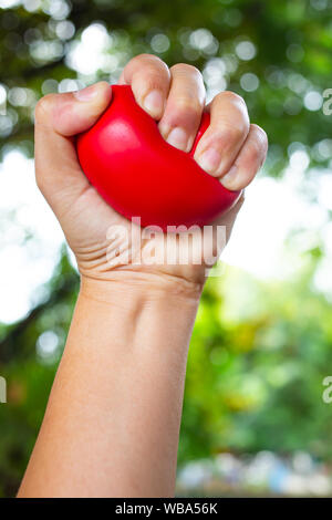 Frau linke Hand zusammendrücken rot Stress Ball auf Bokeh grünen Garten Hintergrund, Übung und Massage Konzept Stockfoto