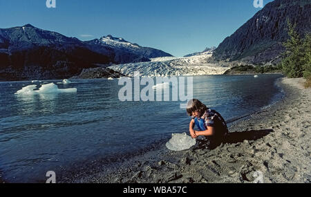 Ein Junge inspiziert einen kleinen Klumpen von schmelzendem Eis, an Land nach dem Weg von einem Eisberg, die aus dem Mendenhall Gletscher, ein Anziehungspunkt für Touristen zu den nahe gelegenen Juneau, der Hauptstadt von Alaska, USA gekalbt hat brechen geschwommen ist. Eine Spur um Mendenhall Lake führt den Besucher näher auf den Gletscher, der bekannteste von 38 großen Gletschern, die von der Weite des Schnee und Eis als Juneau Icefield bekannt. Mendenhall Gletscher zogen sich 2,5 Meilen (4 Kilometer) bis das Tal seit Mitte der 1700er Jahre und das Tempo der Schmelzen steigt aufgrund der globalen Erwärmung. Stockfoto