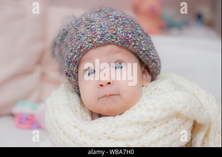 Kleines Kind auf einem Teppich in die graue Schutzkappe. Schönes Portrait. Neugeborenes Baby girl Hintergrund. Winterurlaub Hintergrund. Baby Care. Stockfoto