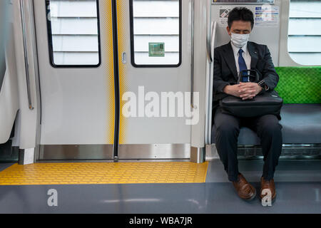 Ein japanischer Büroangestellter oder Salaryman, der eine Gesichtsmaske trägt, schläft in einem Pendlerzug in Tokio, Japan. Stockfoto