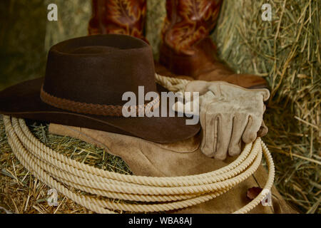 Western lasso mit einem Cowboyhut, leder handschuhe, Cowboystiefel und Leder Chaps auf Heu mit einer geringen Tiefenschärfe Stockfoto