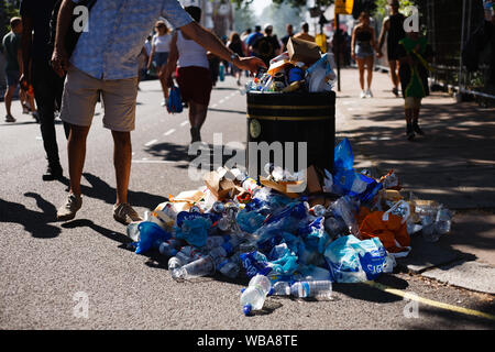 London, Großbritannien. 25 Aug, 2019. Ein Mann fügt ein Stück Müll eine Überfließende bin während der Eröffnung Tag der 2019 Notting Hill Carnival. Bis zu eine Million Menschen werden erwartet, durch die Straßen von Notting Hill zu packen und den umliegenden Gebieten im Laufe der zweitägigen Veranstaltung. Die jährliche Feier des afro-karibischen Kultur nimmt jeder Platz August Bank Holiday Wochenende. Credit: SOPA Images Limited/Alamy leben Nachrichten Stockfoto