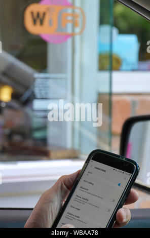 Middletown, CT USA. Jun 2019. Treiber mit Telefon in der Hand einrichten online Zugriff durch Fenster mit Wi-Fi emblem Aufkleber beim Parken. Stockfoto