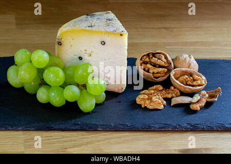 Scheibe frischen landwirtschaftlichen Hartkäse mit Pfeffer und Gewürze, Stillleben mit Walnüsse Trauben und Scheiben Käse. Stockfoto