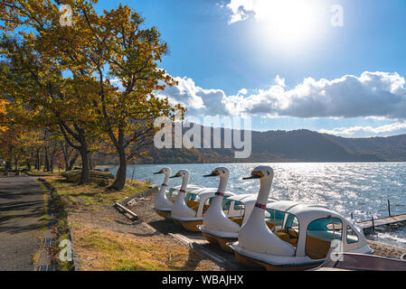 Schönen Herbst Laub Landschaft Landschaften der See Towada in sonniger Tag. Blick vom Lakeside pier, Swan Yachten in den Vordergrund, klarer Himmel, blaue Wasser Stockfoto