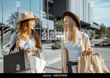 Zwei glückliche Freundinnen gehen mit Einkaufstüten vor der Shopping Mall, zufriedenen Gefühl mit neuen Käufen Stockfoto