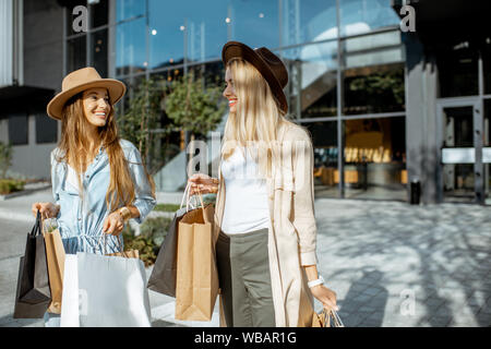 Zwei glückliche Freundinnen gehen mit Einkaufstüten vor der Shopping Mall, zufriedenen Gefühl mit neuen Käufen Stockfoto