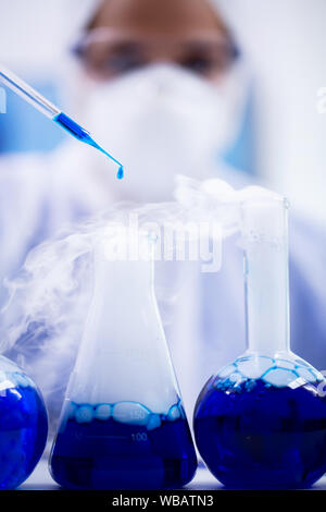 In der Nähe von blauen Lösung fallen von der Pipette in ein Reagenzglas mit Rauchen Flüssigkeit. Wissenschaftler in Schutz. Stockfoto