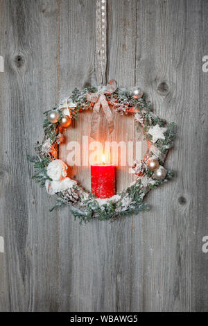 Natürliche Weihnachten Dekoration: Eine brennende rote Kerze in einem Weihnachten Kranz auf eine Holzwand, Schweiz.. Stockfoto