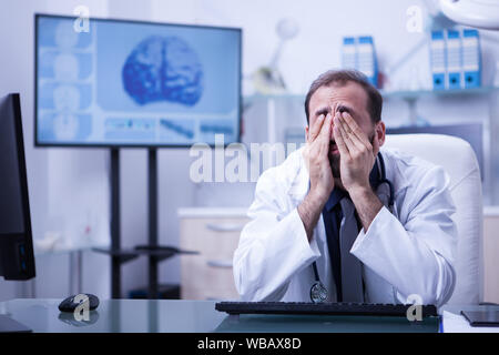 Portrait der junge Arzt seine Augen trägt ein weißes Fell reiben. Müde Arzt im Krankenhaus. Stockfoto