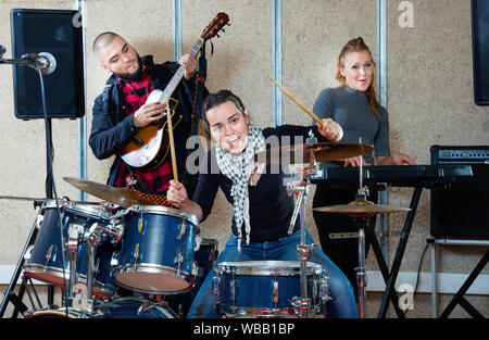 Leidenschaftlich emotionale glücklich, fröhlich lächelnd weibliche Drummer mit ihren Bandkollegen üben im Proberaum Stockfoto