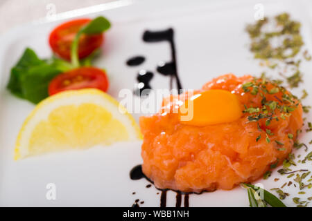 Tartar von frischem Lachs auf weiße Platte. Rezept: fein hacken 200 g Fisch, Würzen sie mit Salz, schwarzem Pfeffer, Olivenöl, Zitronensaft, garniert mit Eigelb Stockfoto