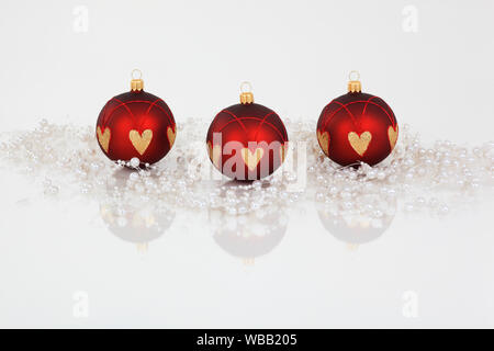 Drei Christbaumkugeln in Rot und Gold, eine Perlenkette umgeben. Studio Bild vor einem weißen Hintergrund. Schweiz Stockfoto