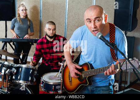 Probe von Music Group. Positive lächelnde Band Leader Gitarre spielen und singen mit seinen Musikern im Studio Stockfoto