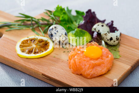 Frischer Lachs Tatar mit Wachtelei und Gewürzen auf Holzbrett Stockfoto