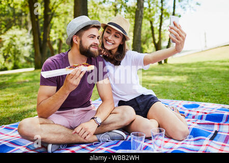 Liebevolle junge Paar essen und unter selfie während auf Picknick im Park Stockfoto