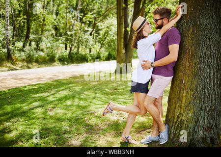 Junge Paare, die in den Park, lehnte sich an einen Baum und an jedem anderen Suchen Stockfoto