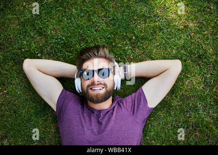 Glückliche Menschen Musik hören, während, die auf dem Gras im Freien und mit Sonnenbrille Stockfoto