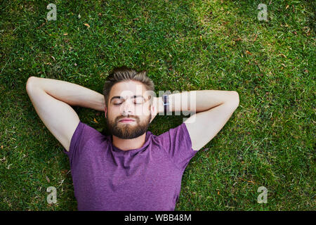 Hübscher junger Mann auf dem Boden liegen und relaxen in den Park mit seinen Augen geschlossen. Stockfoto