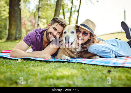 Junges Paar mit Picknick mit ihrem Hund im Park, liegen auf Decke und mit Blick auf die Kamera Stockfoto