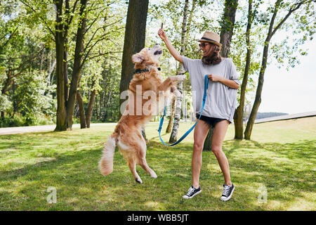 Junge Frau, die das Spielen mit Ihrem Hund auf einen Spaziergang im Park im Sommer Stockfoto