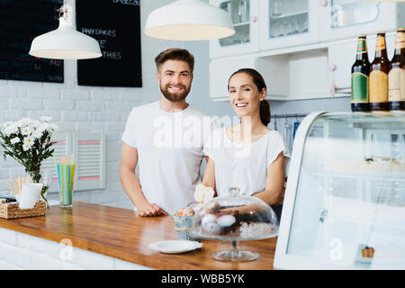 Zwei erfolgreiche Kleinunternehmer starrte auf Kamera und lächelnd steht hinter Zähler in ihrem Restaurant Stockfoto