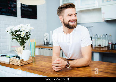 Hübscher junger Restaurant Inhaber lehnte sich auf Zähler und Wegsehen lachen Stockfoto