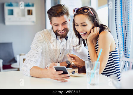 Zwei junge Freunde sitzen zusammen im Café und Suchen am Telefon lachend Stockfoto