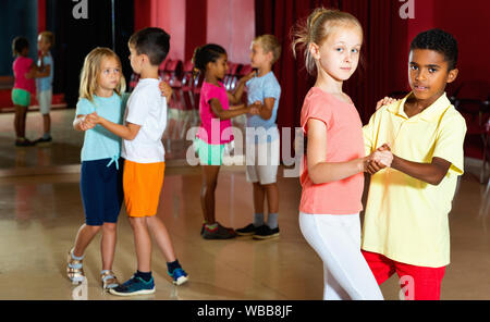 Gruppe von froh lächelnde fröhliche Positiv glückliche Kinder versucht, Tanzen mit Partner im Klassenzimmer Stockfoto