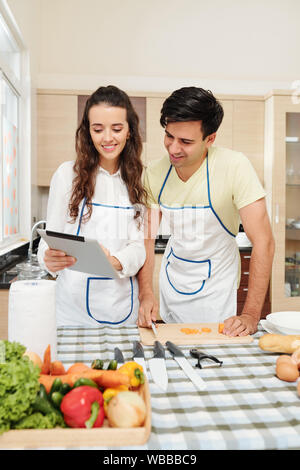 Positive jungen kaukasischen Paar Kontrolle Suppe Rezept auf digitalen Tablet beim Kochen zu Hause Stockfoto