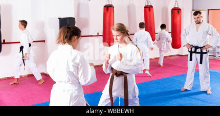 Sorgfältige freundlich lächelnden angenehme Kinder in Kimonos trainieren Techniken, die in Paar während taekwondo Klasse im Gym Stockfoto