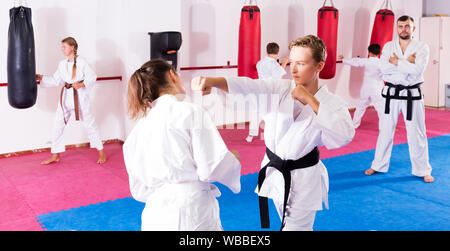 Portrait von aktiven Kindern im Paar Beherrschung neuer Karate bewegt sich während der Gruppe Klasse mit männlichen Trainer Stockfoto