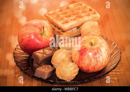 Zwei Äpfel, Waffeln und Süßigkeiten auf braunem Glasplatte. Stillleben Fotografie des Morgen gesundes Frühstück. Stockfoto