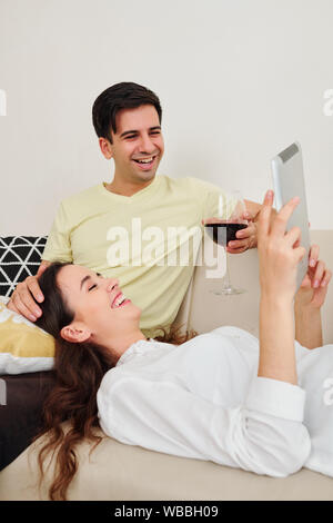 Junge kaukasier Paar ruht auf einem Sofa und Beobachten lustige Komödie Film auf Tablet-PC Stockfoto