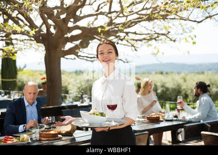 Positive Frau Kellner demonstrieren open-air Restaurant für Besucher Stockfoto