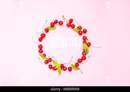 Rahmen aus Süßkirschen auf Licht auf einem rosa Hintergrund. Minimalismus, Flach, Ansicht von oben, Design. Stockfoto