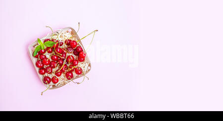 Rote reife Kirschen in einem Weidenkorb auf einem rosa Hintergrund. Stockfoto